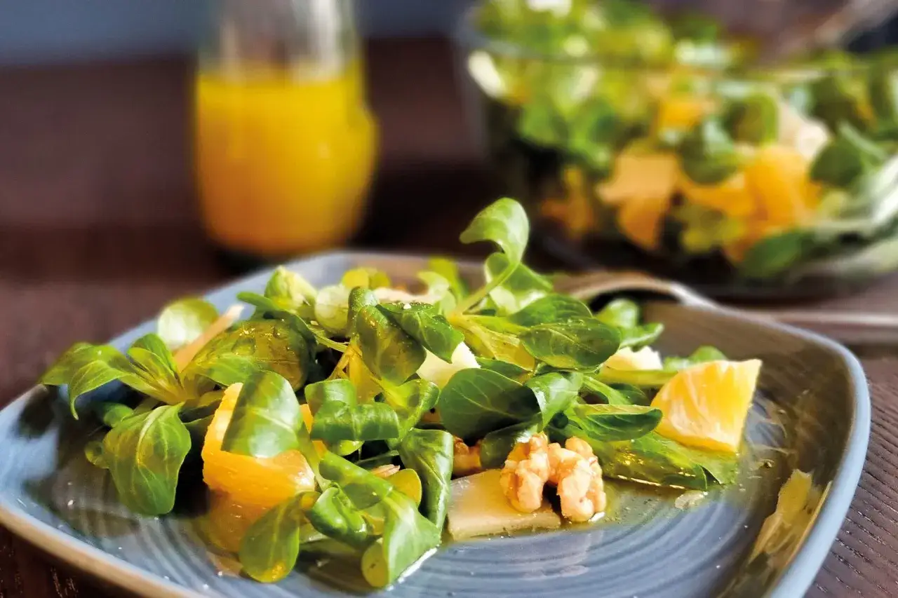 Frischer Feldsalat mit Orangenstücken, Walnüssen und einem leichten Dressing auf einem blauen Teller.