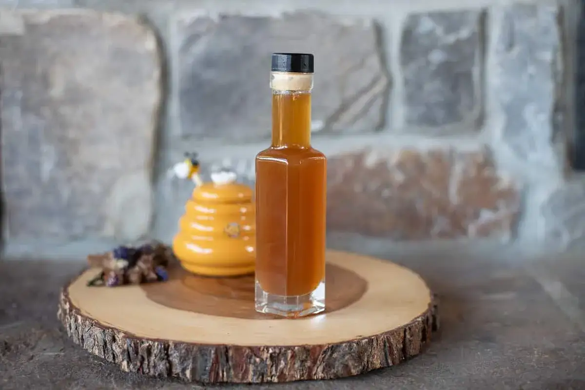 Flasche mit honigbraunem Oxymel, bereit zum Abfüllen. Daneben ein süßer Bienenstock-Dekor.