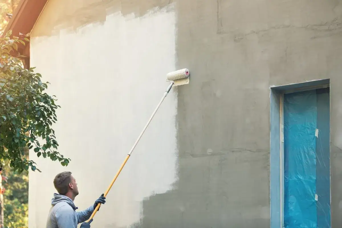 Mann streicht Hauswand mit langem Roller. Kosten für 120 qm Haus streichen im Blick.