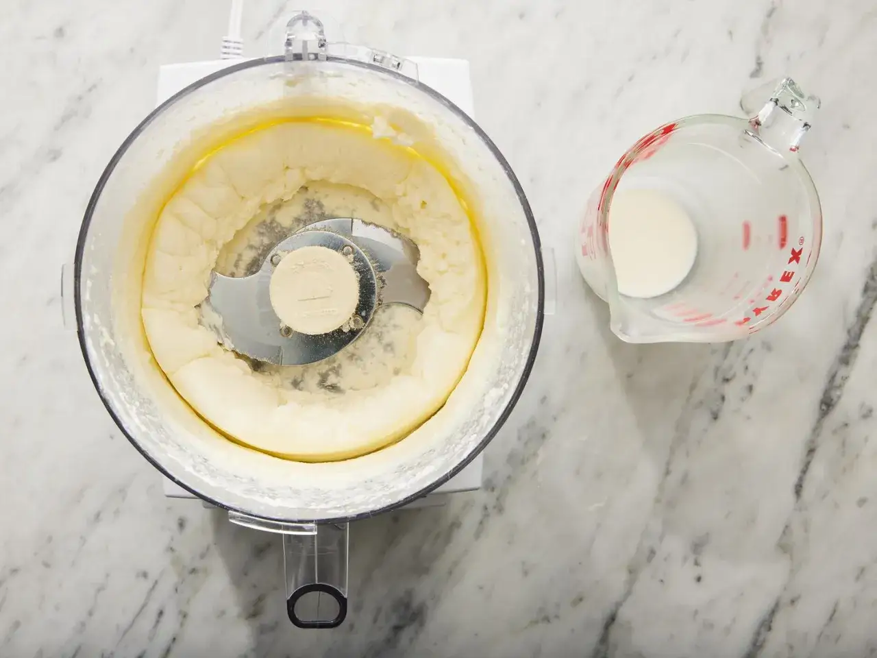 Proceso para como hacer mantequilla casera: nata en procesador de alimentos y jarra medidora con leche.