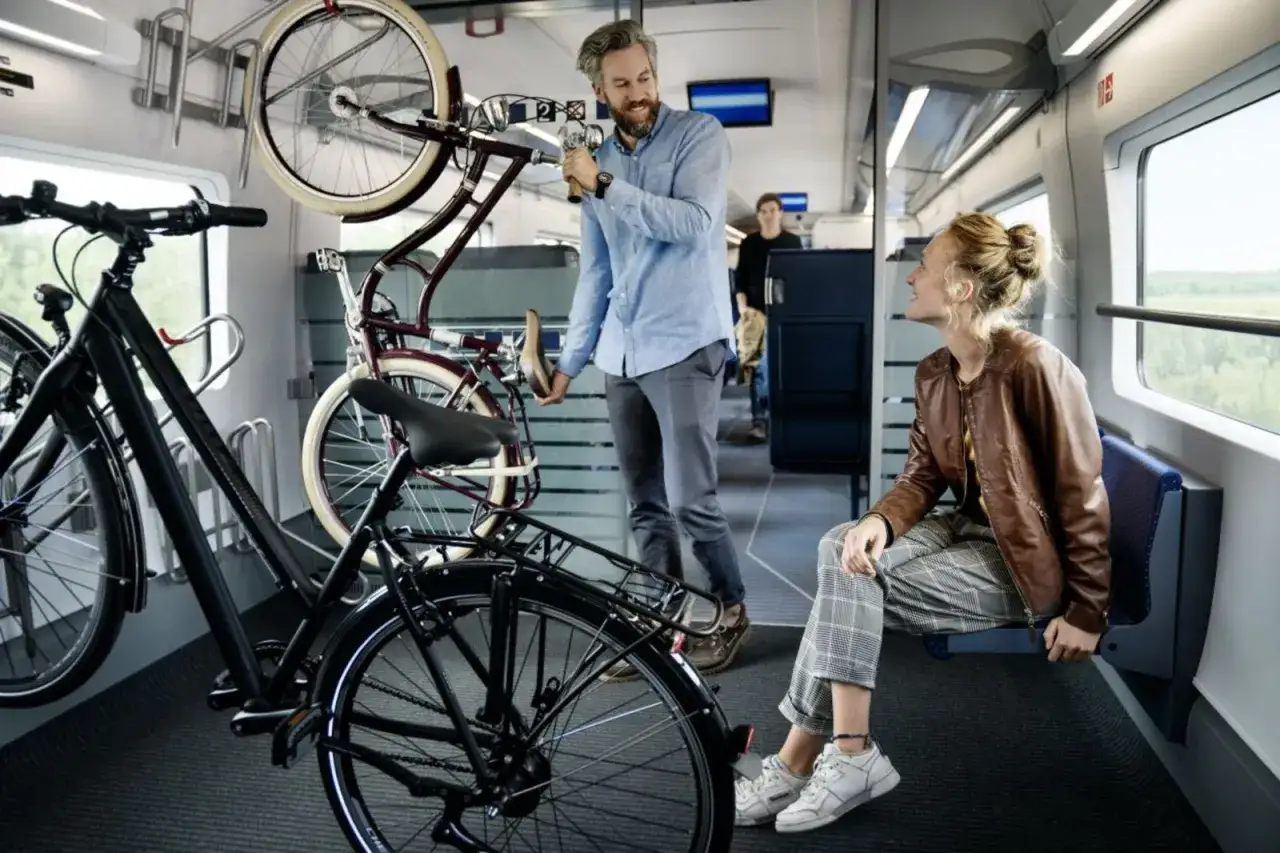 Ein Mann verstaut Fahrräder im ice fahrradabteil. Eine Frau sitzt daneben und schaut aus dem Fenster.