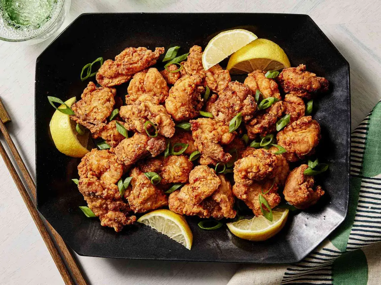 Chrupiący kurczak karaage na czarnym talerzu, udekorowany plasterkami cytryny i szczypiorkiem. Idealna przekąska.