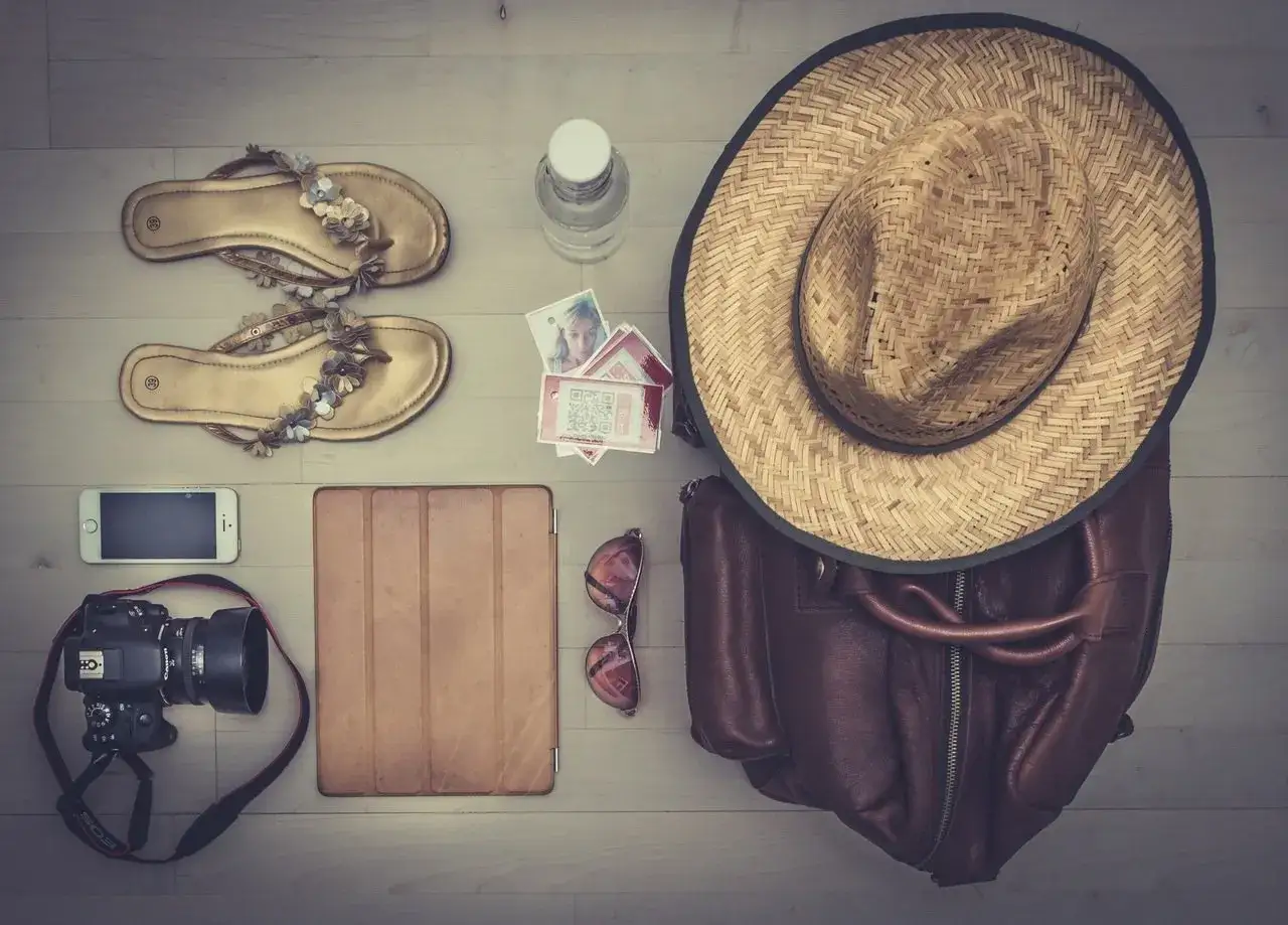 Goldene Sandalen, Kamera, Tablet, Sonnenbrille, Hut und Tasche – alles Reise-Must-Haves für den perfekten Urlaub.