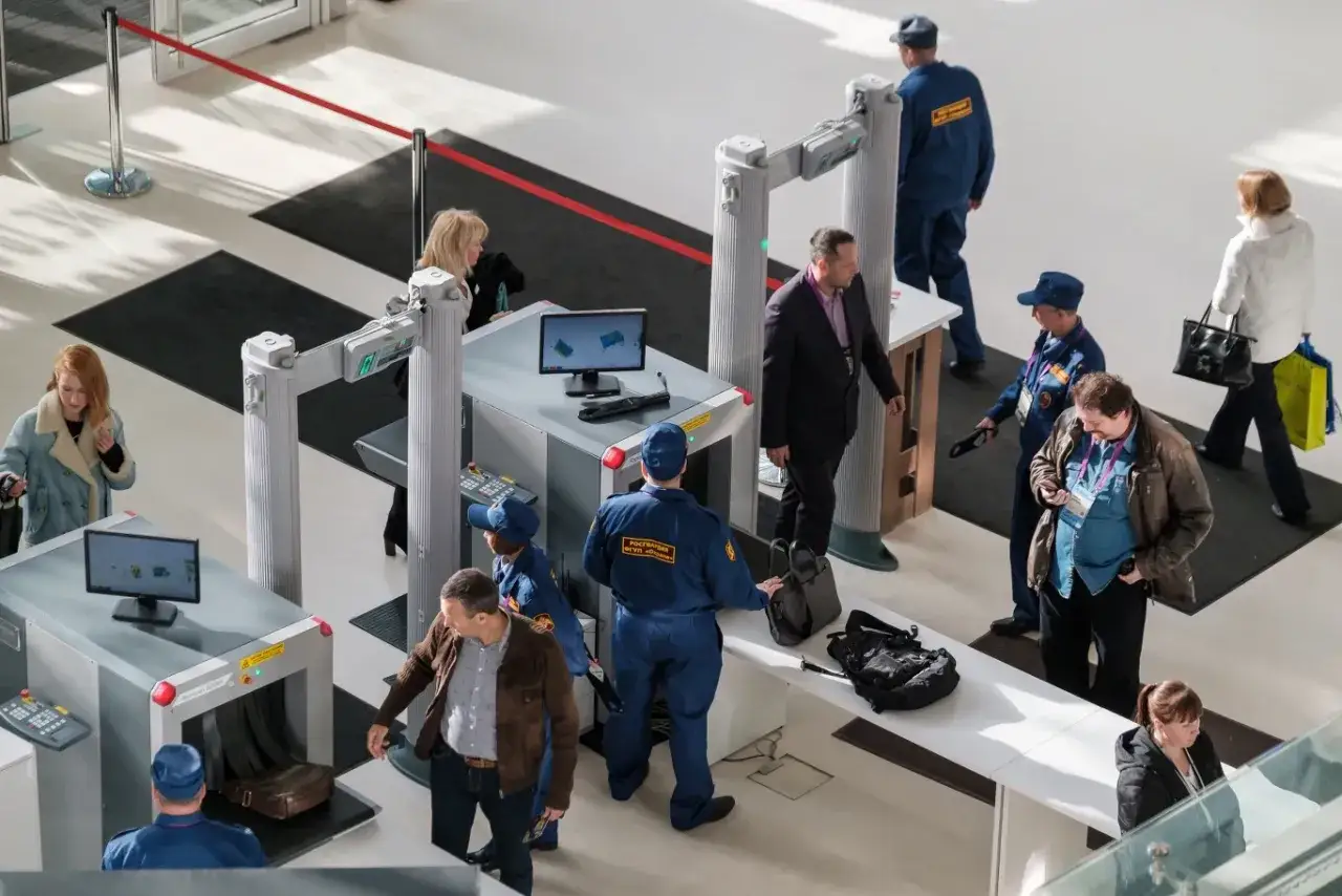 Osoby przechodzą przez bramki na lotnisku, gdzie pracownicy ochrony sprawdzają bagaże i pasażer&oacute;w. Tak działają bramki na lotnisku.