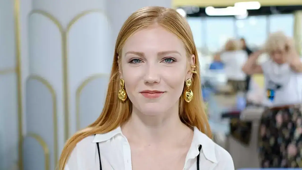 Marianna Kowalewska w białej koszuli i złotych kolczykach, z niebieskimi oczami, uśmiecha się do obiektywu.