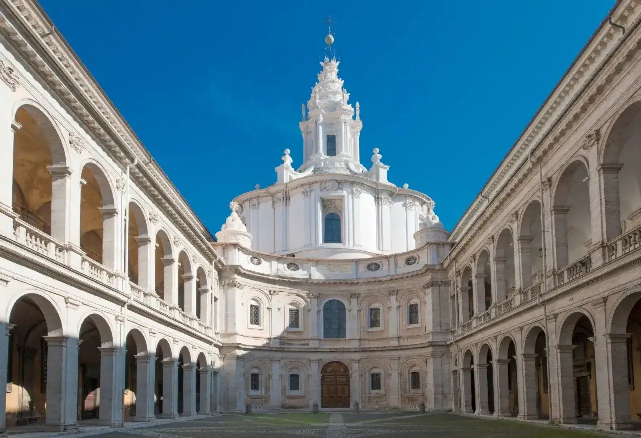 La chiesa della Sapienza a Roma, con la sua imponente cupola e i portici eleganti, si staglia contro un cielo azzurro intenso.