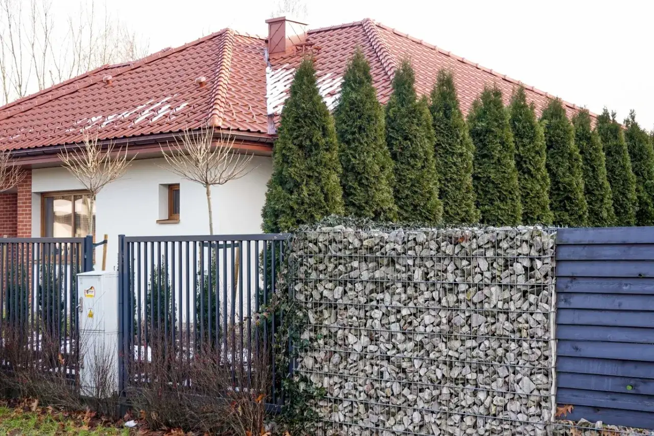Zła brama może uniemożliwić odbiór domu po 20 września 2026. Widok na dom z czerwonym dachem, ogrodzenie z gabionów i żywopłotem.
