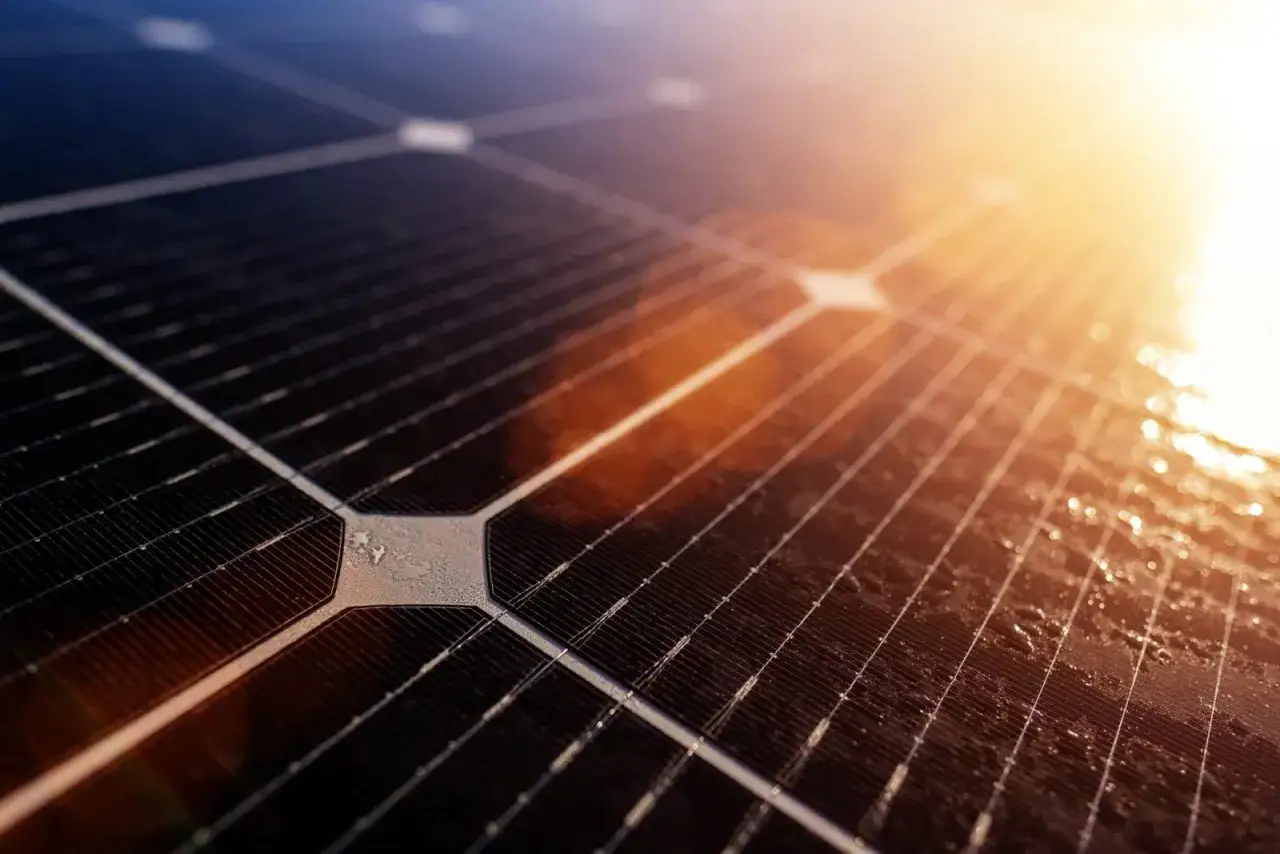 Zbliżenie na panel słoneczny z widocznymi ogniwami. Słońce odbija się od powierzchni, tworząc ciepłe refleksy. To przyszłość energii, być może z wykorzystaniem perowskitu.