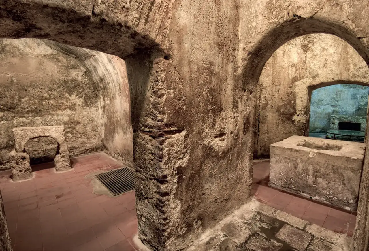 Interno dell'ipogeo San Salvatore: archi in pietra grezza, vasca in cemento e un antico altare.