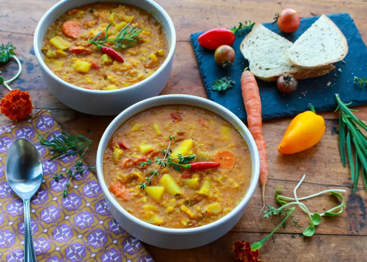Deux bols de soupe de lentilles corail, garnie de romarin et de piment. Une recette réconfortante avec des carottes, des pommes de terre et des tomates.