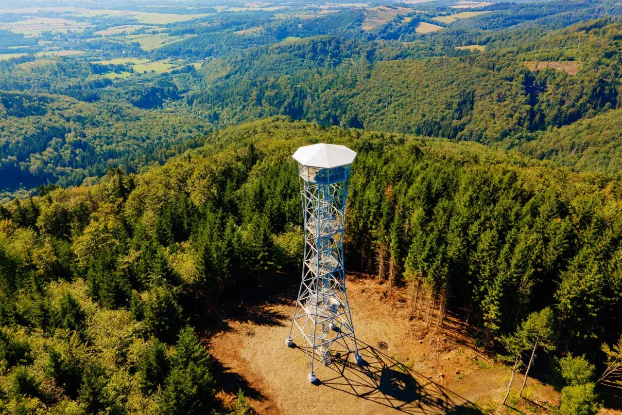 Wieża widokowa na Kłodzkiej Górze pośród gęstego lasu. Rozległa panorama doliny i wzgórz w tle.