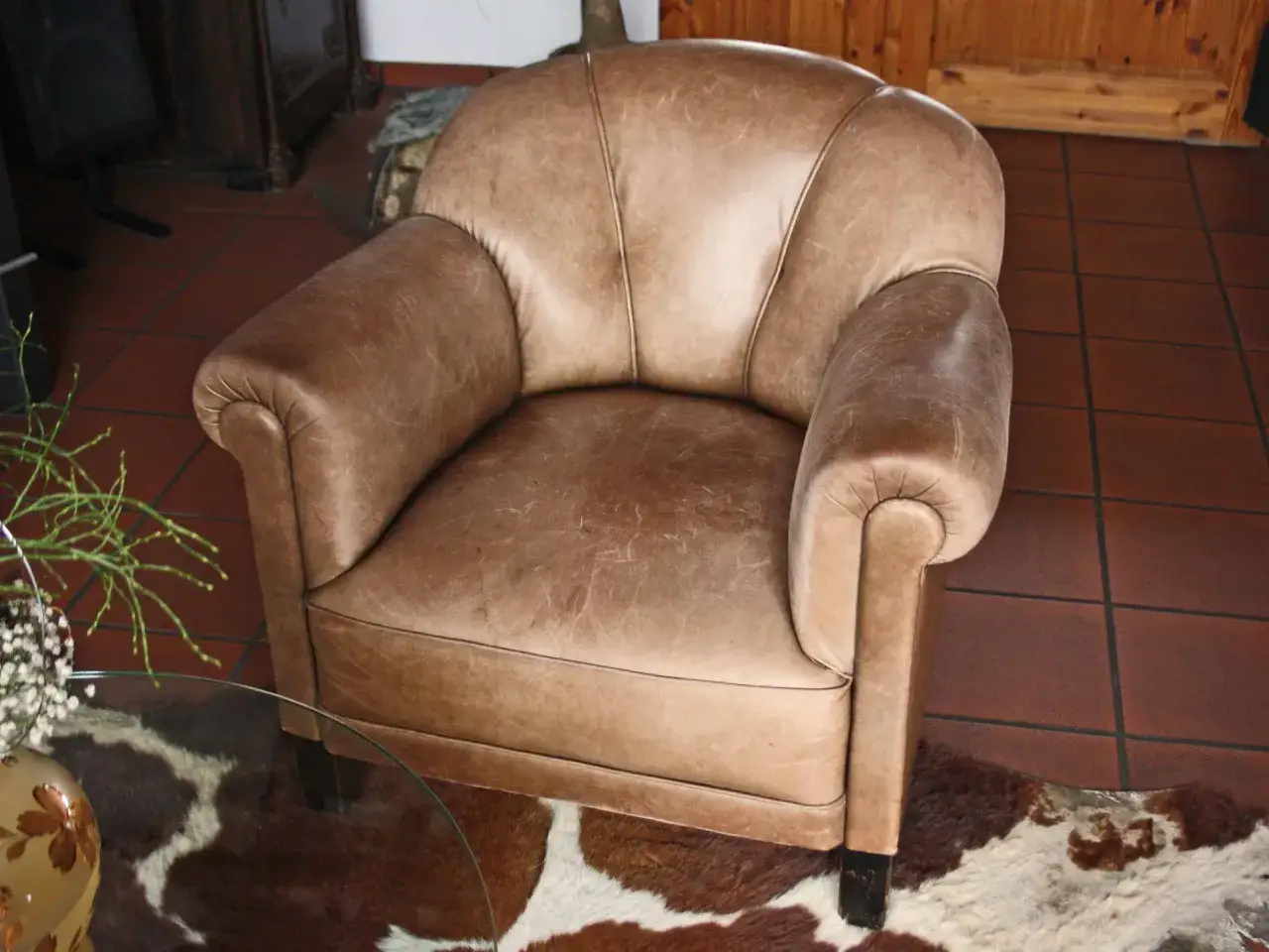 Fauteuil club confortable en cuir aniline patiné, posé sur un tapis peau de vache.