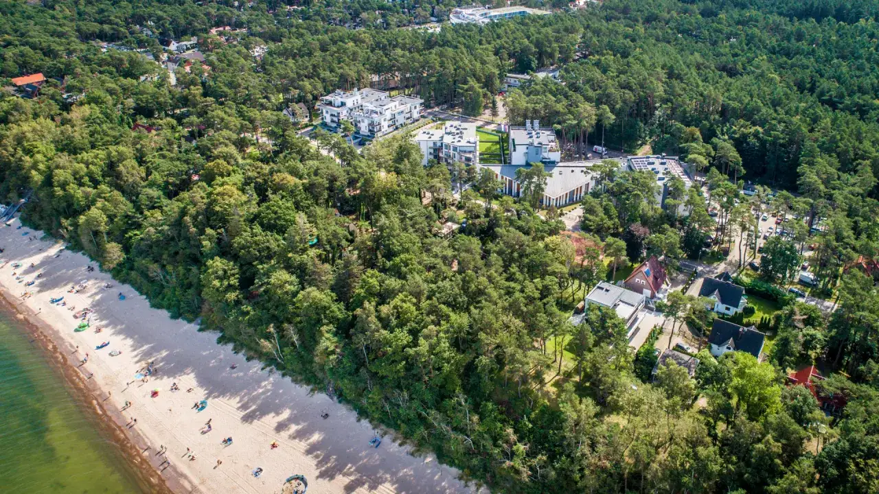 Pobierowo holiday resort: nowoczesne budynki i domki wśród sosnowego lasu, z piaszczystą plażą i morzem w tle.