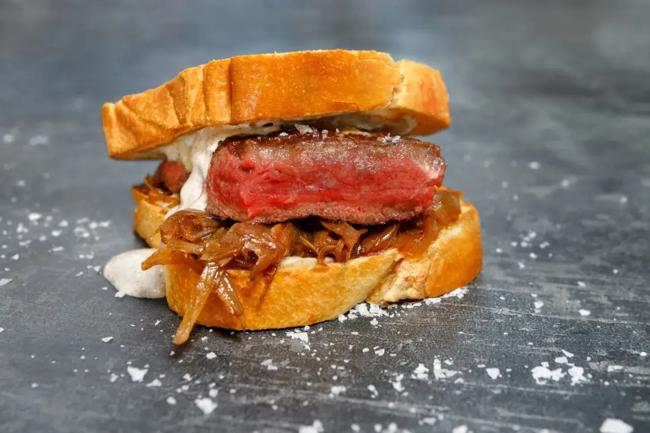 A juicy pepito de ternera, a steak sandwich on toasted bread with caramelized onions and creamy sauce, sprinkled with sea salt.