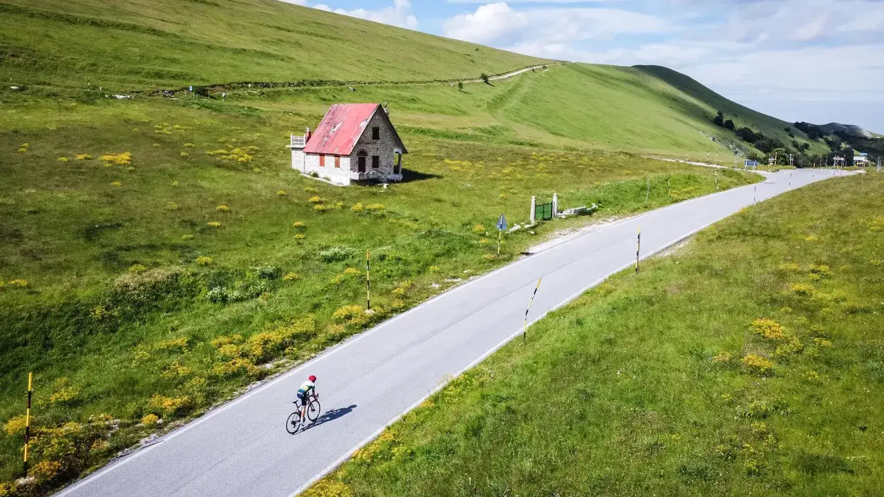 Ciclista solitario su strada panoramica nel Montefeltro. Un'oasi verde con casetta isolata, ideale per scoprire cosa vedere in questa terra di storia e natura.