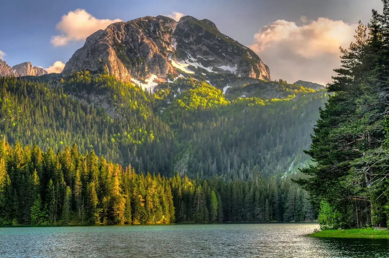 Majest&auml;tische Berge im Durmitor Nationalpark, bedeckt mit Nadelw&auml;ldern und einem glitzernden See im Vordergrund.