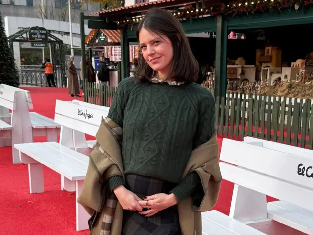 Isabelle Junot sonr&iacute;e en un mercado navide&ntilde;o, con un jersey verde y una bufanda a cuadros.