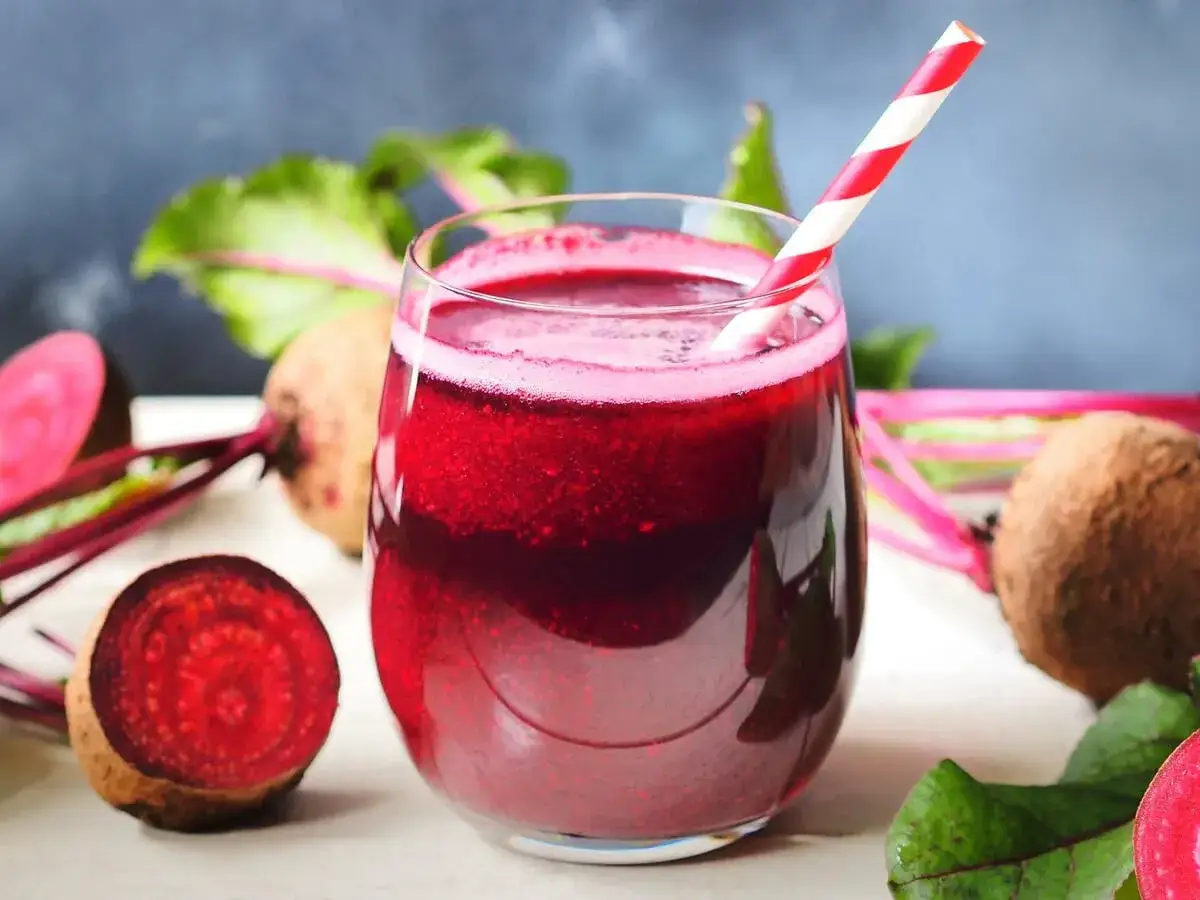Frisch gepresster Saft aus roter Bete in einem Glas mit Strohhalm, umgeben von ganzen und halbierten Rote-Bete-Knollen.