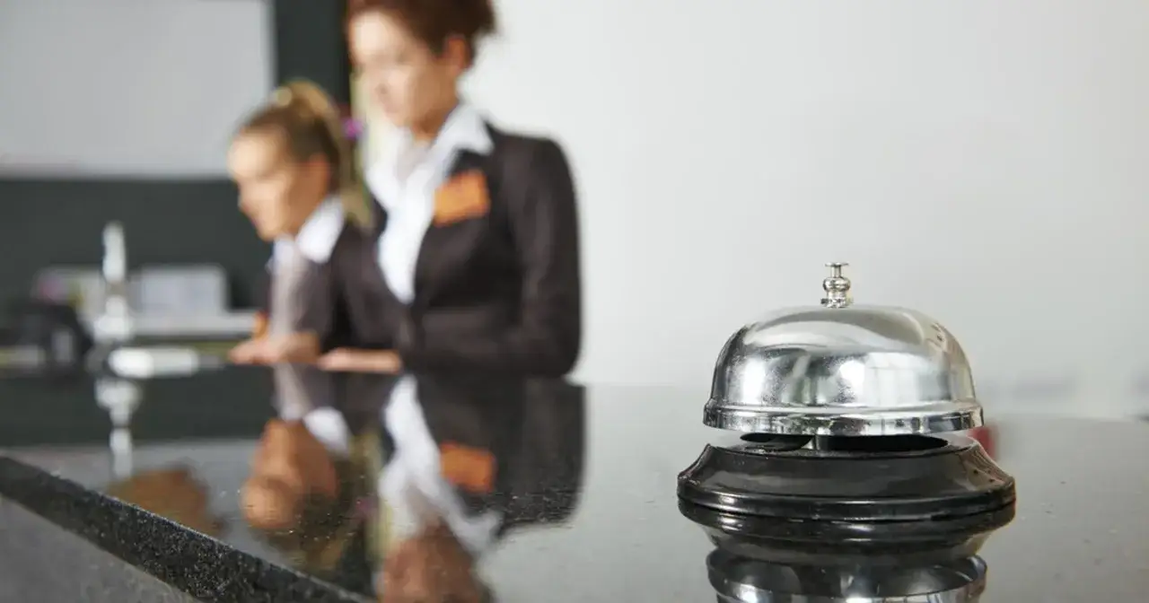 Dwie recepcjonistki w hotelu, jedna z nich dzwoni dzwonkiem. Zastanawiasz się, ile zarabia hotelarz?