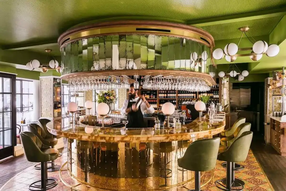 Barman préparant un cocktail dans un bar chic aux murs verts et au comptoir doré. Une ambiance de 