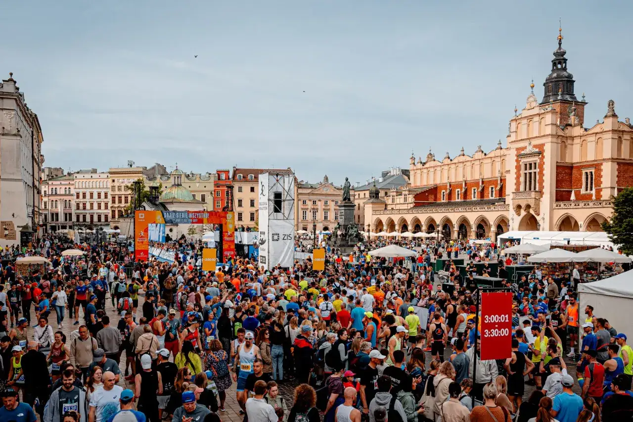 Tłum biegaczy na Rynku Głównym w Krakowie przed startem maratonu. W tle Sukiennice i Brama Floriańska.