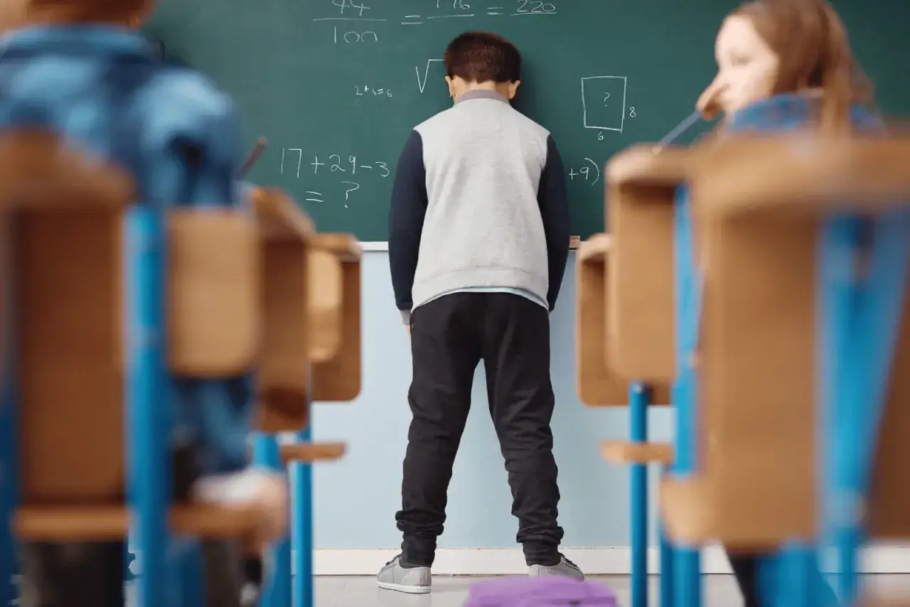Chłopiec stoi przed tablicą, czując lęki u dziecka 7 latka. Matematyka wydaje się przytłaczająca.