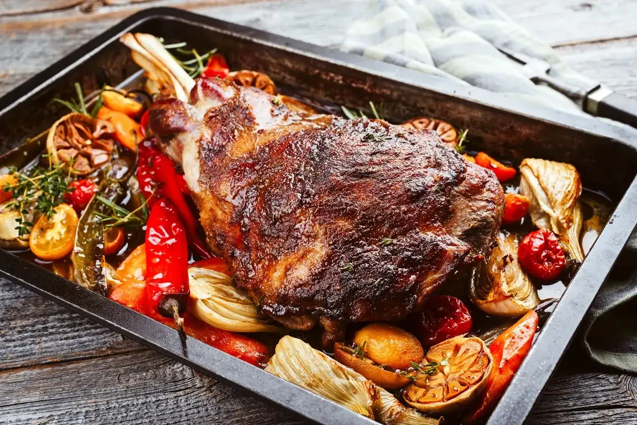 Un gigot d'agneau de 7 heures, rôti à la perfection avec des légumes colorés, des herbes et des citrons confits dans un plat de cuisson.