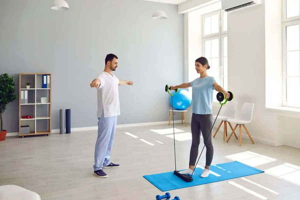 Fizjoterapeuta nadzoruje ćwiczenia rehabilitacyjne pacjentki z użyciem taśm oporowych.