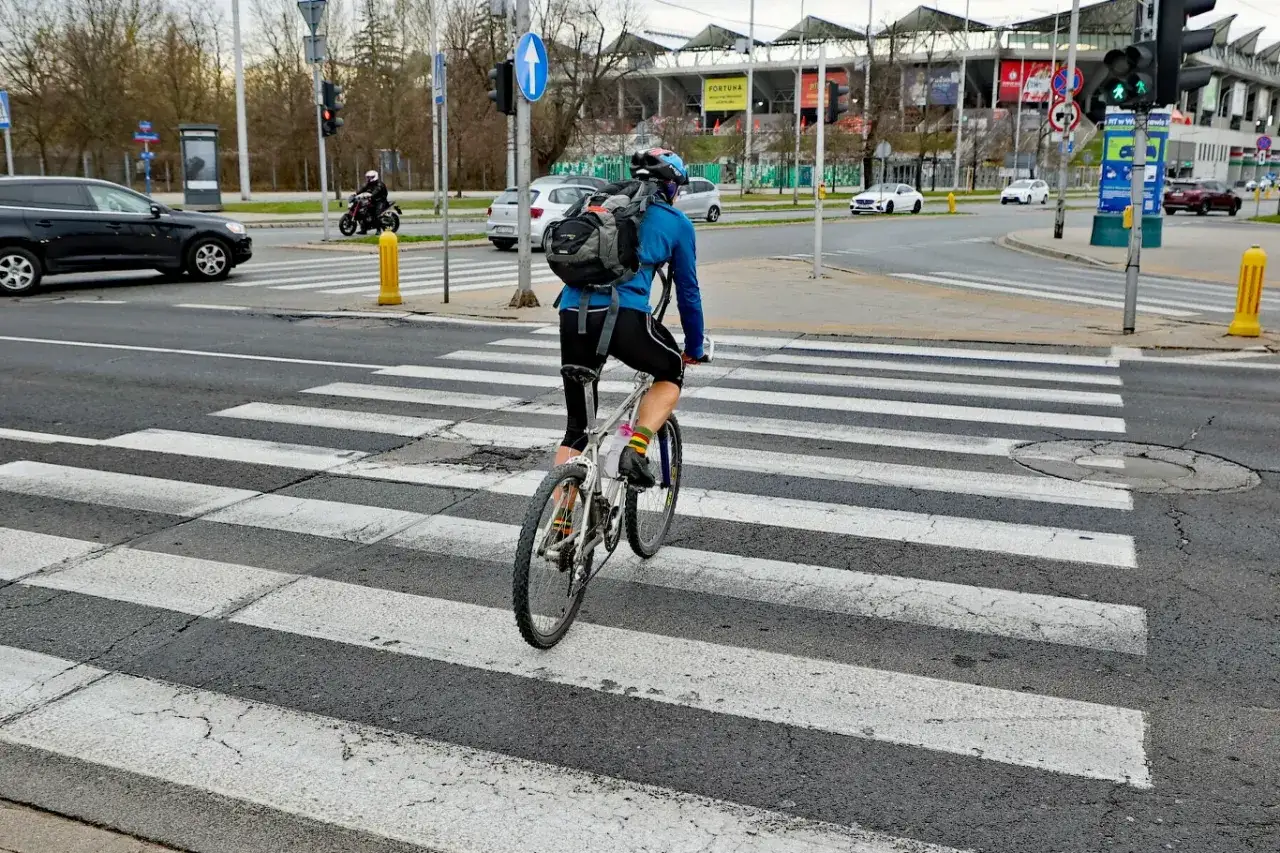 Rowerzysta na pasach. Czy rower to pojazd mechaniczny? Dookoła ruch samochodowy i miejska infrastruktura.
