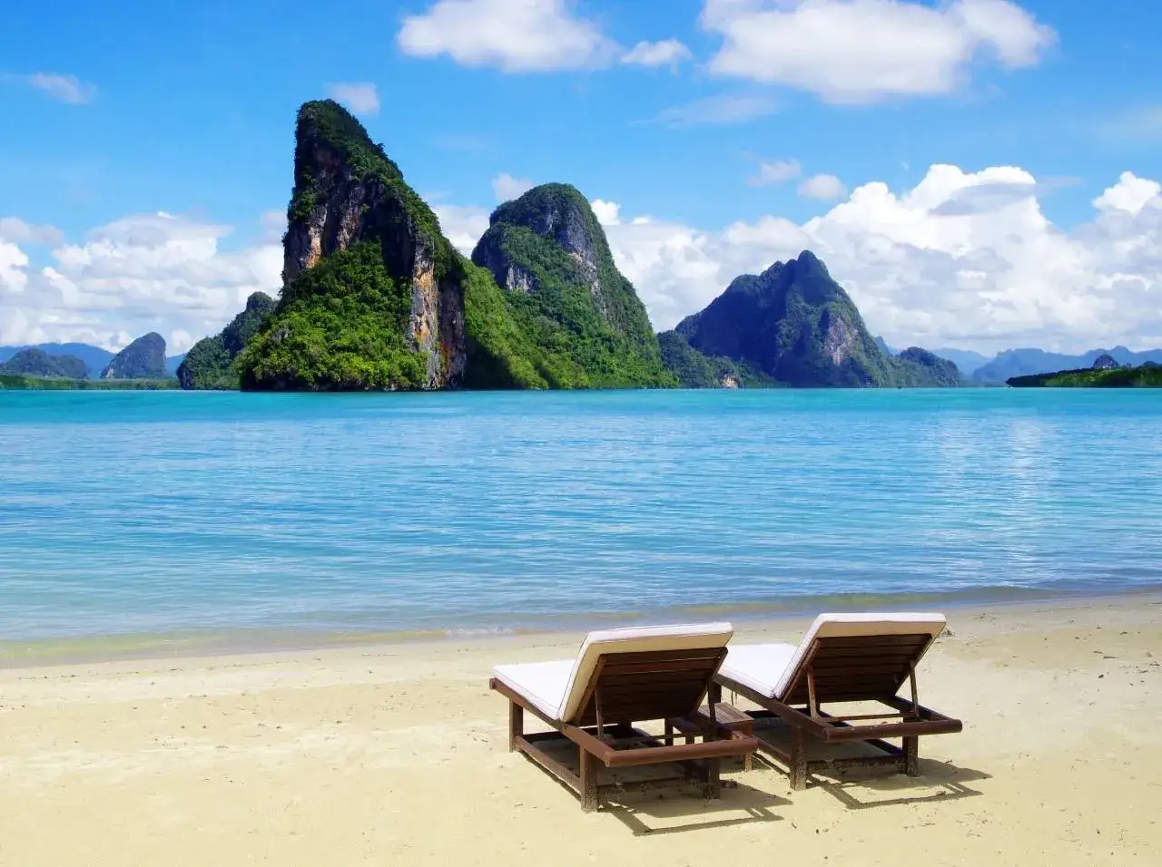 Dwie leżaki na piaszczystej plaży, w tle turkusowe morze i zielone, skaliste wyspy. Idealne krabi atrakcje dla relaksu.