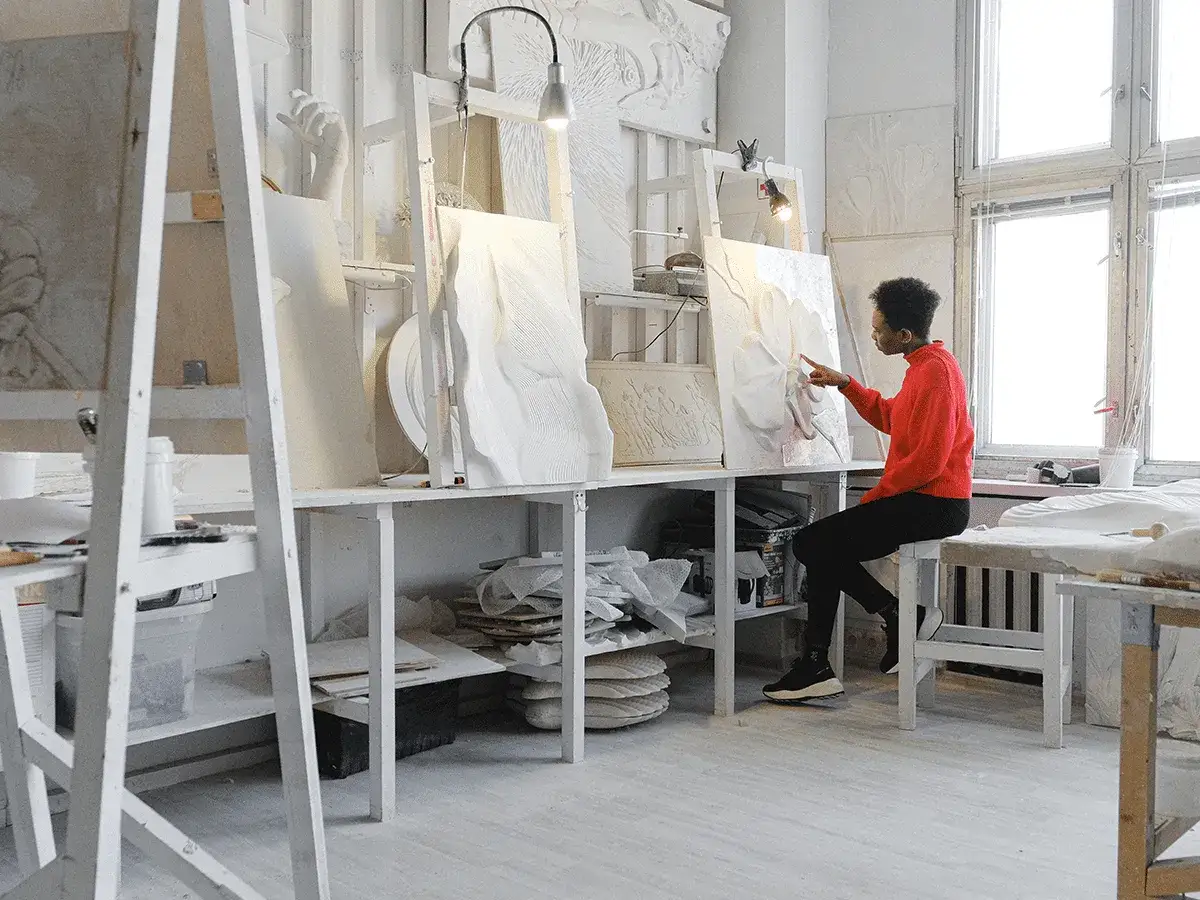 Une artiste examine une sculpture en relief, se demandant quelle peinture pour toile conviendrait le mieux à son œuvre.