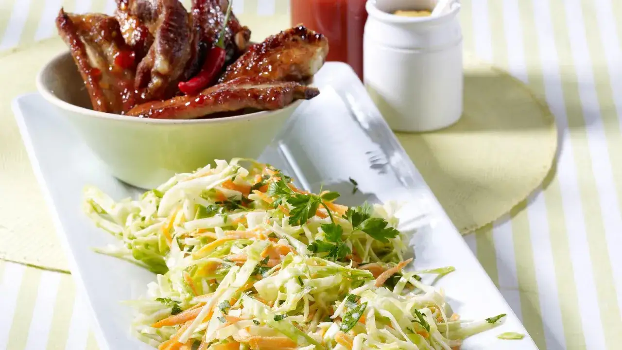 Saftige Spareribs mit einem frischen Krautsalat, garniert mit Petersilie. Ein perfektes Duo für den Sommer.