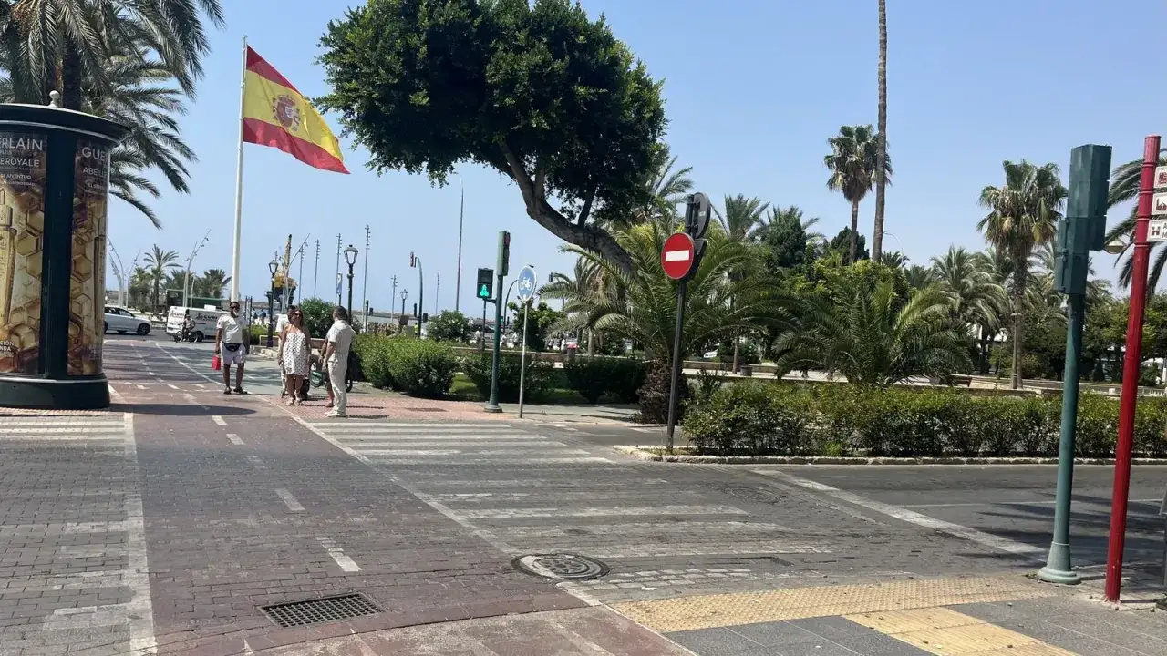 Bandera española ondea en la rambla de Almería, con palmeras y gente paseando.