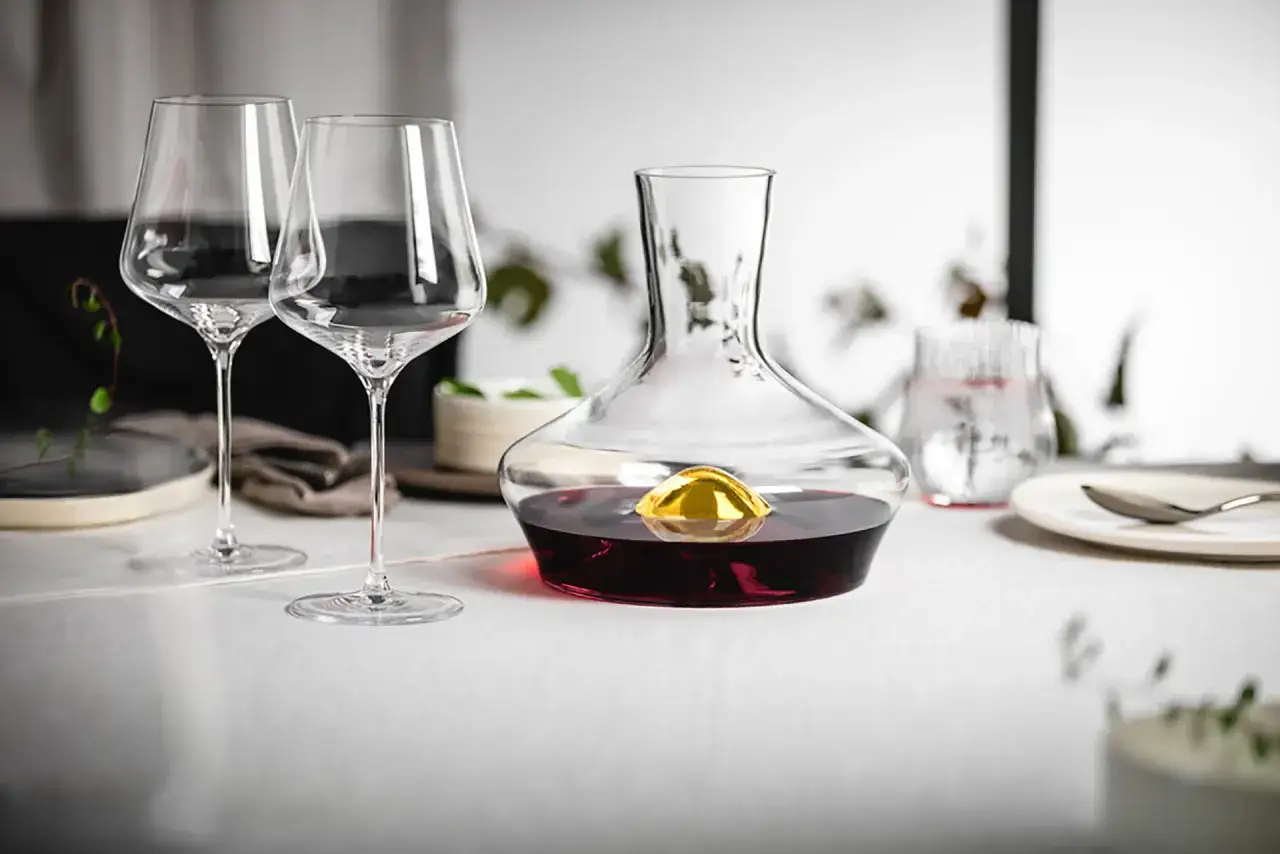 Elegancka karafka z czerwonym winem i złotą kulą, obok dwa kieliszki. Idealne na degustację wina, ale wermut co to? To aromatyzowane wino, często podawane jako aperitif.