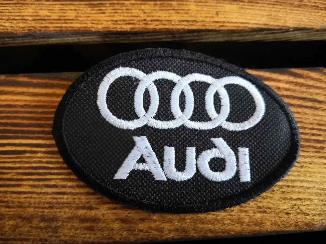 Naszywka z białym emblematem Audi na czarnym tle, idealna do personalizacji odzieży lub akcesoriów.