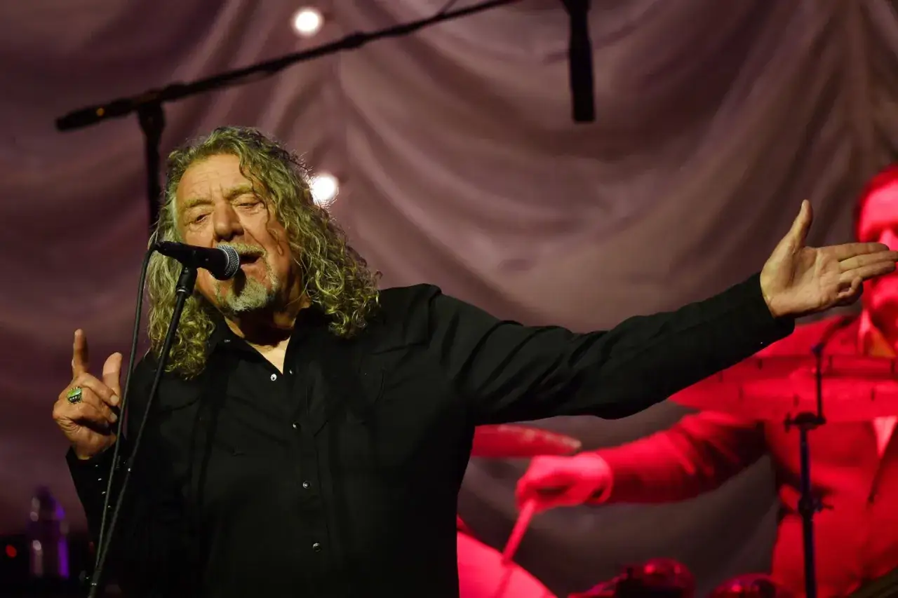 Wokalista Led Zeppelin, Robert Plant, śpiewa do mikrofonu, gestykulując ręką.