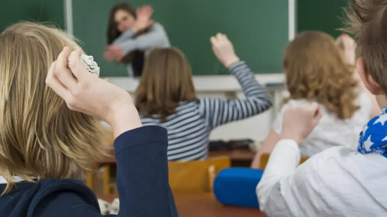 Sch&uuml;ler werfen Papierkugeln, w&auml;hrend eine Lehrerin versucht, die Situation zu beruhigen. Dies zeigt die Notwendigkeit von Strategien gegen Mobbing.