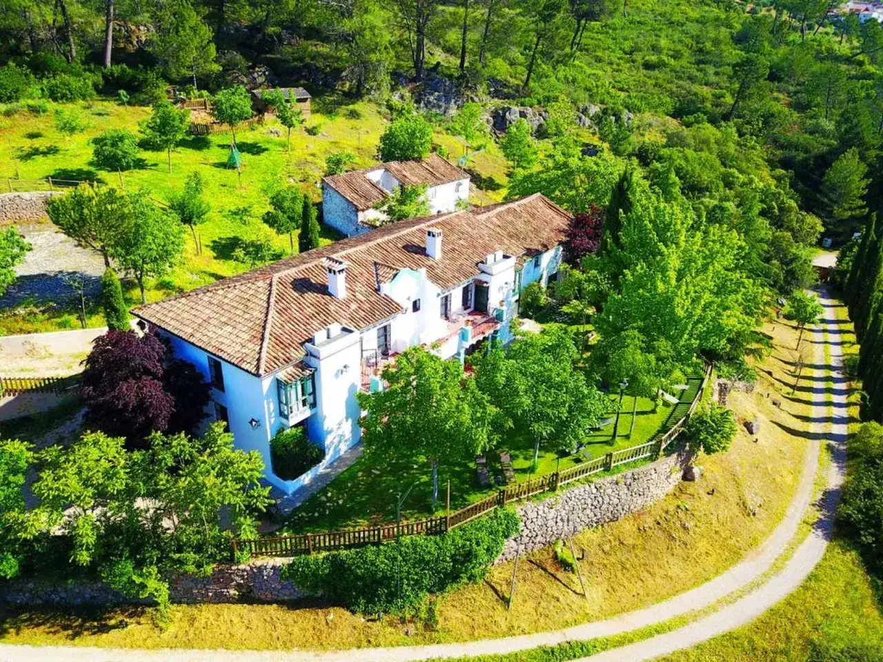 El cortijo los pradillos, una casa blanca con tejado de tejas, rodeada de exuberante vegetación y árboles frondosos.