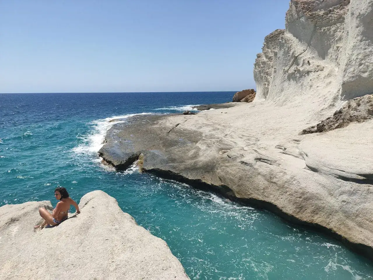 Una persona descansa en la roca de la cala del medio, con el mar turquesa y acantilados blancos de fondo.