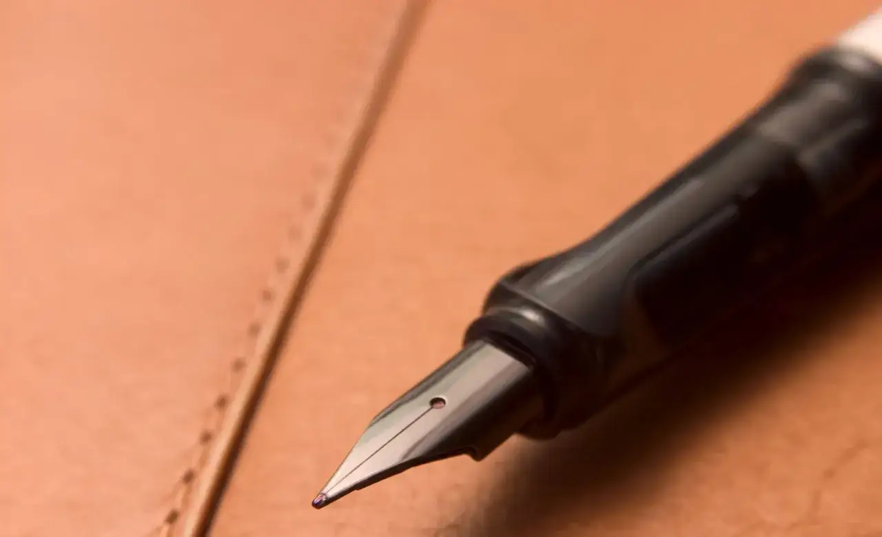 Plume d'un stylo plume noir sur un cuir brun. Une tache d'encre ? Apprenez comment enlever du stylo sur du cuir.
