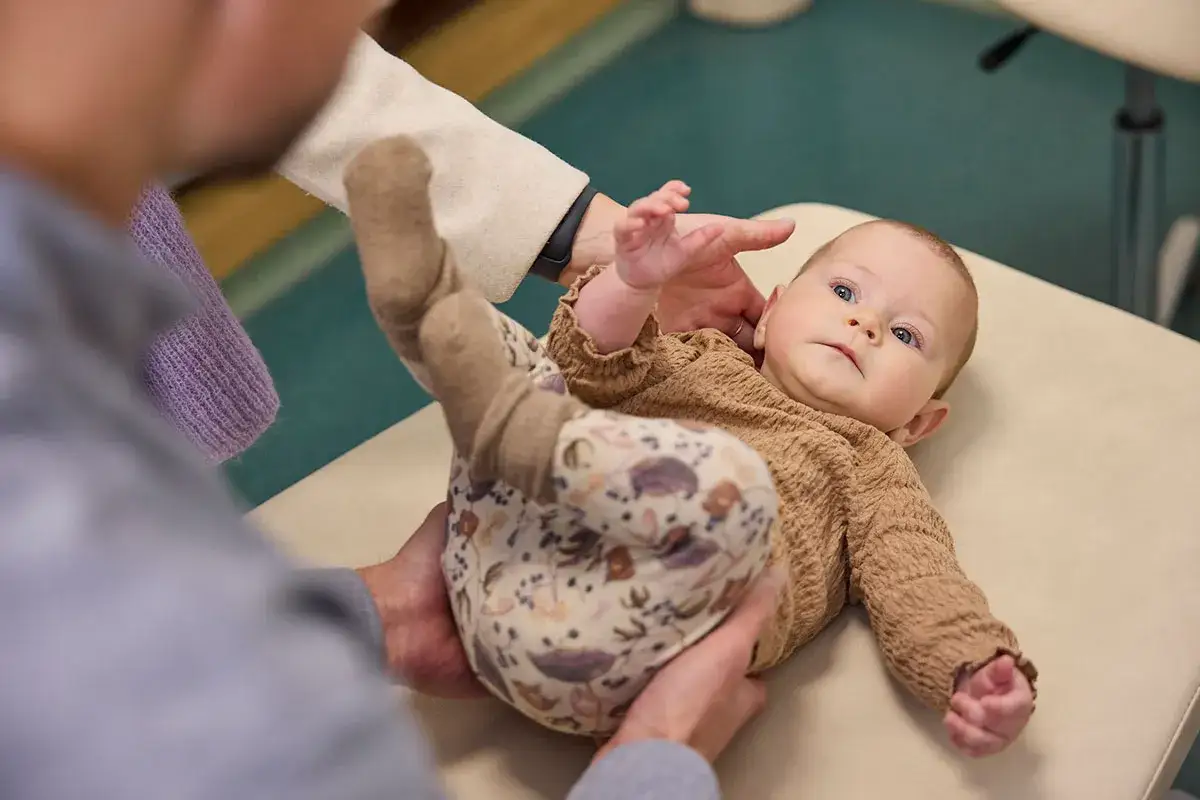 Ein Baby liegt auf einer Liege, die H&auml;nde eines Osteopathen st&uuml;tzen es. Das Kleine wirkt entspannt und zufrieden, fast wie ausgewechselt nach der Behandlung.