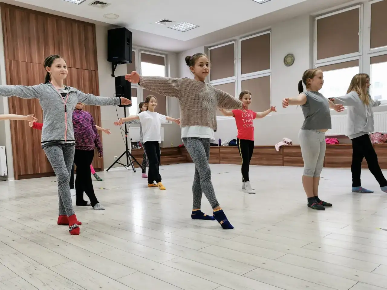 Dziewczynki ćwiczą naukę tańca, rozciągając ramiona w sali lekcyjnej.