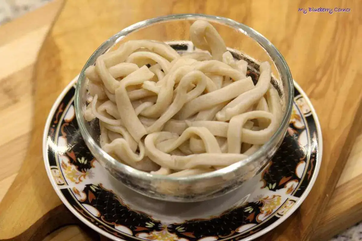 Grube, białe kluski makaronu udon w szklanej misce, gotowe do przygotowania według przepisu.