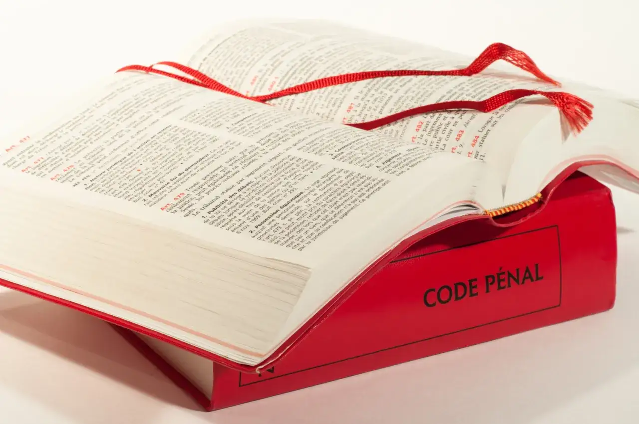 Un Code pénal rouge ouvert, avec un ruban rouge. L'article 311-1 du code pénal est visible.