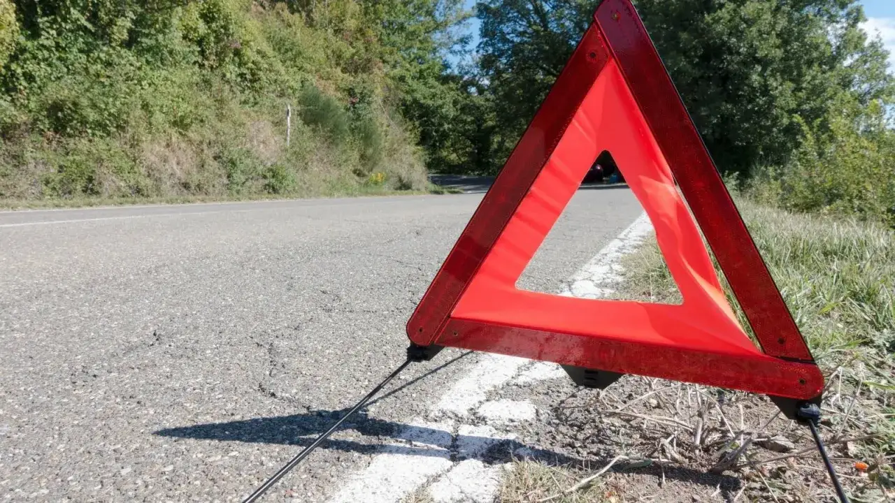 Czerwony trójkąt ostrzegawczy odległości stoi na poboczu drogi, sygnalizując awarię.