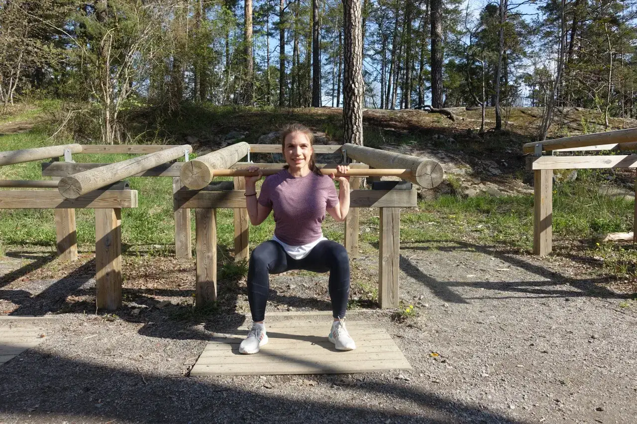 Kvinna g&ouml;r kn&auml;b&ouml;j med en stock p&aring; en utomhus tr&auml;ningsplats. Street workout i skogen.