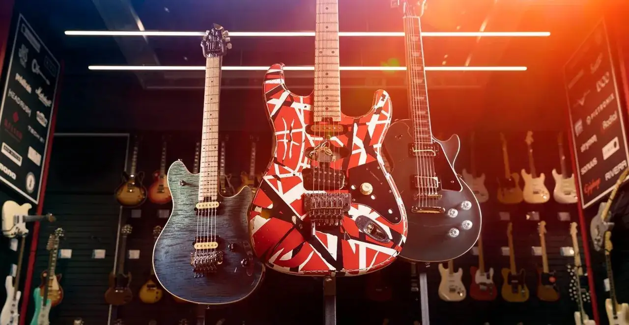 Tre chitarre iconiche: una blu fiammata, una rossa e bianca stile Van Halen e una nera Les Paul. La scelta tra Les Paul vs Stratocaster è un dilemma per ogni chitarrista.