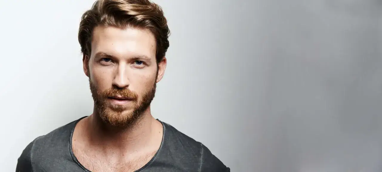Ein Mann mit markanten blauen Augen und einem l&auml;ssigen 3-Tage-Bart tr&auml;gt ein graues T-Shirt.