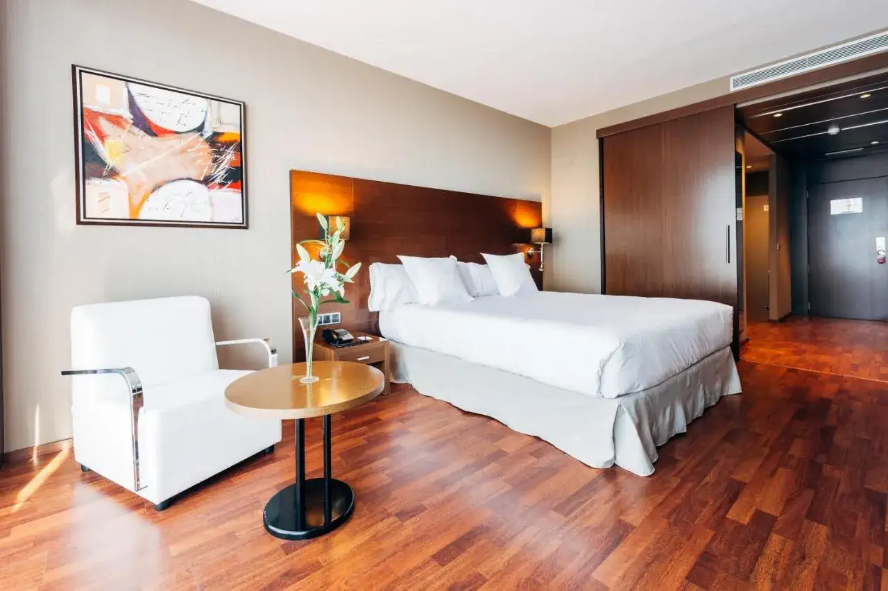 Habitación de lujo en Azz Valencia Congress Hotel & Spa. Cama doble, sillón blanco, mesa auxiliar y obra de arte abstracta.