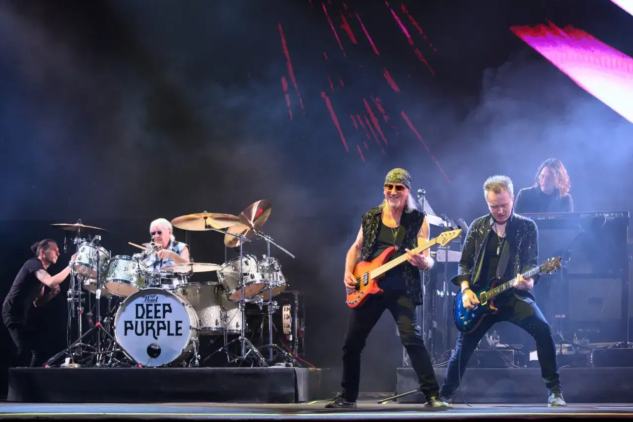 Członkowie Deep Purple na scenie: basista z pomarańczową gitarą, gitarzysta z niebieską gitarą, perkusista i klawiszowiec.